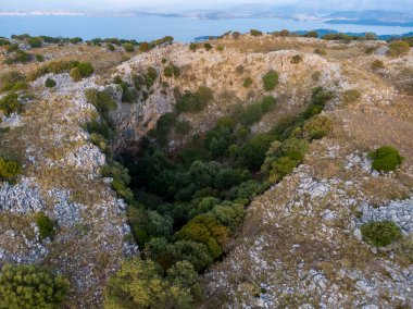 Aerial view of a sinkhole filled with lush vegetation, contrasting with the rocky landscape. clipart