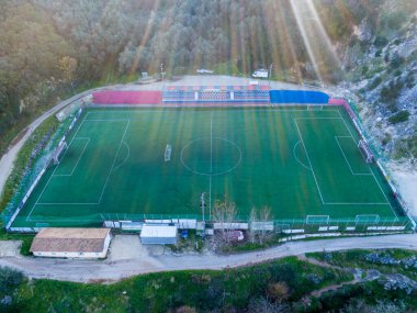 Yamaçtaki bir futbol sahasının havadan görünüşü. Güneş ışınları akarak yeşil bölgeyi aydınlatıyor..