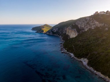 Sahil kayalıkları ve sakin okyanus suları berrak bir gökyüzünün altında buluşur. Doğanın güzelliğinin pitoresk bir görüntüsü.