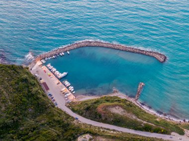 Sahil limanı, tekneler ve temiz su, yukarıdan görüldü. Tepe boyunca manzaralı bir yol esiyor..