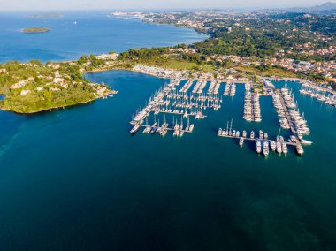 Yat ve yelkenlilerle dolu bir marinanın havadan görünüşü, manzaralı bir sahile yerleşmiş..
