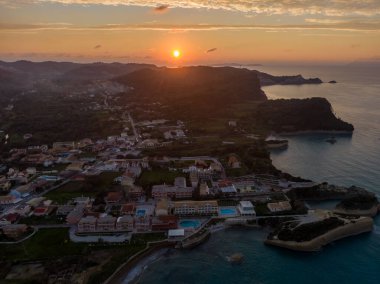 Sahil kasabasında gün batımı, hava manzarası. Altın saat ışığı binaları ve turkuaz denizi yıkıyor..