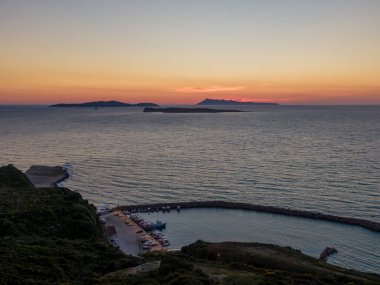 Sahil limanında gün batımı ve uzak adalar. Sakin bir tekne ve sakin sular manzarası.