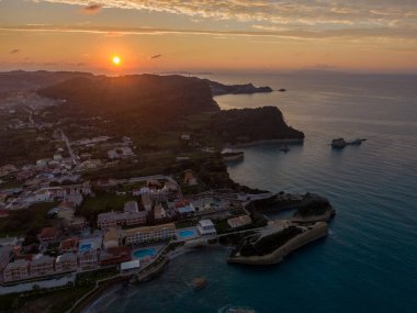 Tepeler ve deniz arasında yuva yapmış bir kasabanın üzerinde sahil gün batımı. Altın saat ışığı sahneyi sıcak tonlarda yıkar..