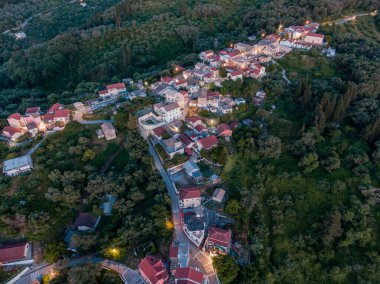 Alacakaranlıkta yemyeşil bir yamaçta yuva yapmış büyüleyici bir köyün hava manzarası..