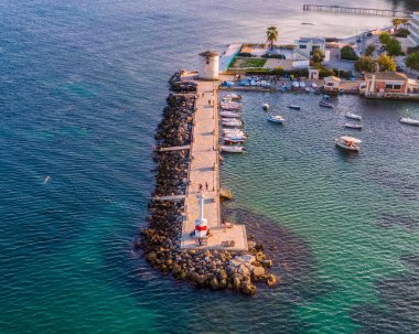 Yel değirmeni ve tekneleri olan sahil iskelesi. Yüzücülerle ve temiz suyla sakin deniz manzarası.