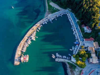 Teknelerle dolu, yemyeşil ağaçlarla dolu bir sahil şeridi boyunca uzanan pitoresk bir limanın havadan görünüşü..