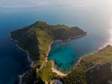 Etrafı yemyeşil tepelerle çevrili turkuaz suyu olan tenha bir körfezin havadan görünüşü..