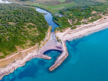 Bir nehrin denizle buluştuğu sakin bir kıyı koyunun havadan görünüşü. Bereketli yeşillik ve kumlu plaj görülebilir..