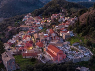 Alacakaranlıkta tepedeki köy, yeşil tepelerin arasına kurulmuş aydınlık evler. Huzurlu, huzurlu bir sahne..