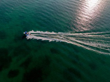 Koyu bir deniz mavisi okyanusunda hızla ilerleyen bir motorlu teknenin havadan görünüşü beyaz bir iz bırakıyor..