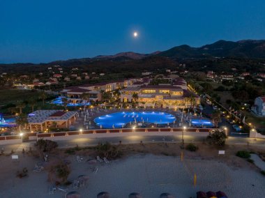 Kumsala yakın bir tatil köyünün gece manzarası, bir dağ zeminine ve dolunaya karşı aydınlatılmış..