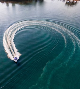 Sürat teknesi, derin mavi bir göl boyunca dairesel bir yol kazıyor, arkasında beyaz bir iz bırakıyor..
