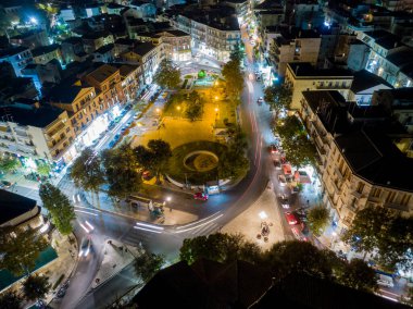 Trafik ve binalarla dolu bir şehir meydanının gece manzarası. Aydınlatılmış sokaklar ve yuvarlak yollar.