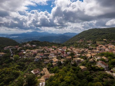 Hilltop village nestled in a lush landscape, with mountains and sea in the distance. clipart