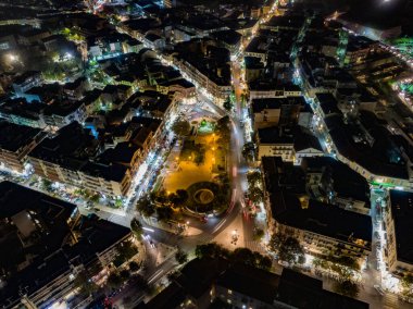 Sokak lambalarıyla aydınlatılmış şehir meydanının ve etrafındaki sokakların gece hava görüntüsü..