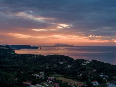 Huzurlu bir denizin üzerinde, önünde tepeler ve binalar olan sahil günbatımı. Huzurlu bir akşam sahnesi.