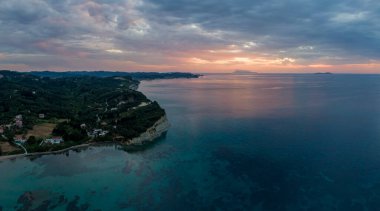 Yeşil tepeli ve sakin okyanus sularıyla sahil gün batımı manzarası. Seyahat ve doğa meraklıları için mükemmel bir manzara..