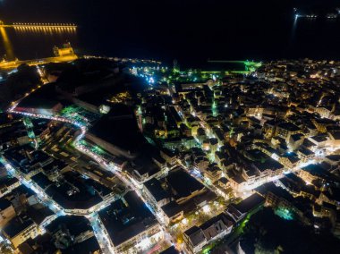 Gece manzaralı hava manzarası. Aydınlatılmış sokaklar ve binalar, uzakta bir liman.
