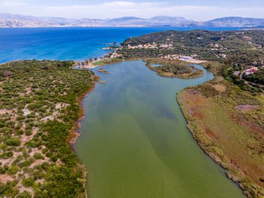 Bereketli yeşillik ve sakin deniz arasında yuva yapmış bir lagünün havadan görünüşü, uzaktaki dağlar..