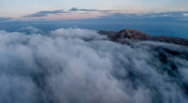 Dağ zirvesi sisle kaplanmış, yukarıdan sakin bir manzara..