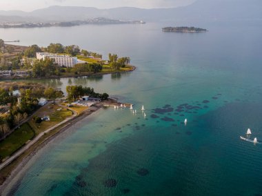Yelkenli ve berrak suları olan sahil beldesi. Huzurlu bir körfezin manzarası. Bir tatil köyü, marina ve yelkenli sergileniyor..