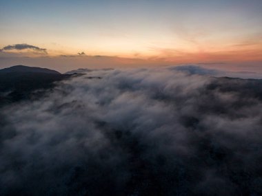 Bulutlar ve dağlardan oluşan bir denizin üzerinde gün doğumu. Yukarıdan nefes kesici bir manzara.