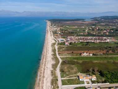 Çarpıcı bir kıyı şeridinin havadan görünüşü, turkuaz su, sahil gelişimi ve uzak dağlarla desteklenen kumlu sahille buluşur..