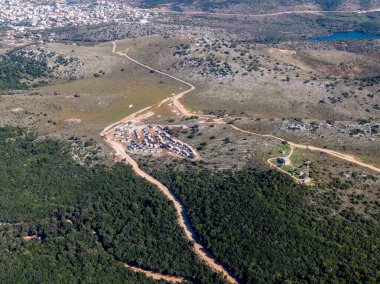 Dağlık bir araziye yerleşmiş, seyrek bitki örtüsü ve sık ormanlardan geçen yolların bulunduğu kırsal bir yerleşim alanının havadan görünüşü..