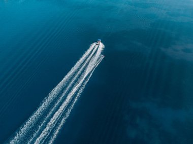 Sakin mavi bir göl üzerinde, bir teknenin hava görüntüsü bir uyanış yaratıyor. Arkasında tek başına bir su kayağı..