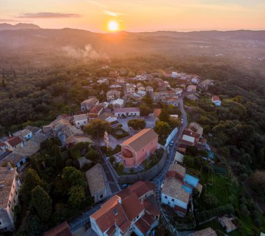 Büyüleyici bir yamaç köyünün üzerinde gün batımı. Sıcak altın ışık geleneksel taş evleri ve çevreleyen tepeleri yıkıyor..