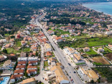 Etrafı evler ve yeşil alanlarla çevrili uzun bir yol boyunca uzanan kıyı kasabasının havadan görüntüsü..