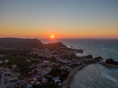 Sahil kasabasının günbatımı hava manzarası. Güneş ufkun altına batarken turuncu renkler gökyüzünü boyuyor. Binaları ve denizi aydınlatıyor..