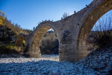 Kuru bir nehir yatağının üzerinde kadim taş köprü, huzurlu bir manzaraya yerleşmiş..