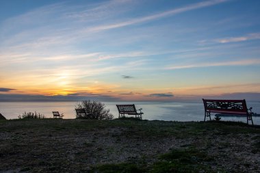 Uçurumun tepesinden gün batımı manzarası, sakin denize bakan üç bank. Huzurlu bir düşünce için mükemmel..