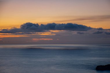 Okyanusun üzerinde dramatik bulutlarla gün batımı. Huzurlu ve huzurlu kıyı manzarası.