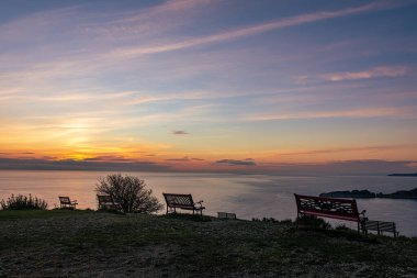 Sakin bir deniz manzaralı, sakin bir tepeden gün batımı manzarası. Birkaç bank manzaranın tadını çıkarmak için huzurlu bir yer sunuyor..