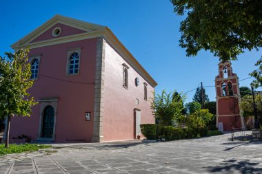 Açık mavi gökyüzünün altında çan kulesi olan pembe kilise binası. Sakin bir sahne..