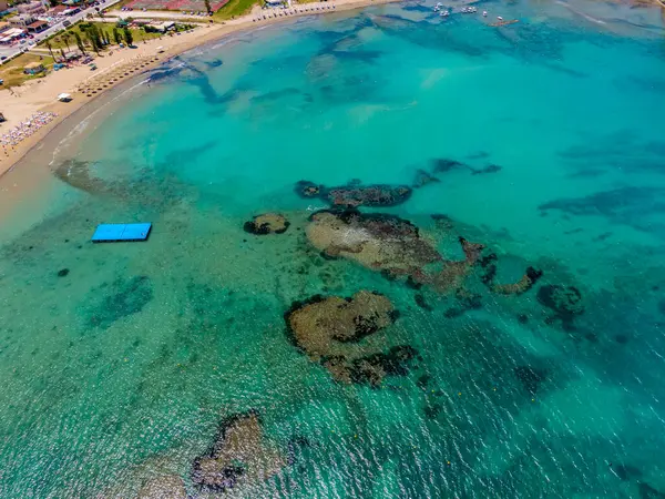 Sersemletici bir turkuaz plajın havadan görünüşü berrak su altında kayaları ve kumlu bir sahili ortaya çıkarıyor..