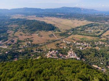 Yeşil tepelerin ve uzak dağlara kadar uzanan tarlaların arasında yuva yapmış bir köyü gösteren sakin bir manzara..