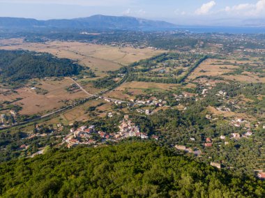 Bereketli yeşillikler ve tarım arazileri arasında yuva yapmış sakin bir deniz manzaralı bir sahil kasabasının havadan görünüşü..
