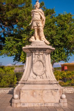 Tarihsel bir heykel, yemyeşil yemyeşil ve taştan bir tabanla çevrili güneşli bir parkta dimdik duruyor..