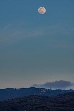 Dolunay alacakaranlıkta bir dağ sırasının üzerinden yükseliyor..