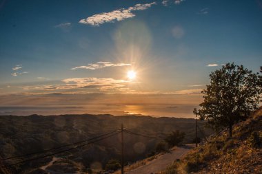 Yuvarlanan tepelerin üzerinde gün batımı ve sakin bir deniz