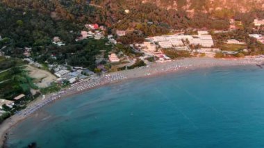 Şemsiyeli sahil beldesi, temiz su ve arka planda tepeler, Yunanistan 'ın Korfu adasındaki Kontogialos plajı.