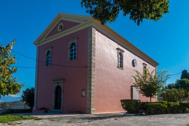 Açık mavi gökyüzünün altında, saat ve kemerli pencereli pembe bina..