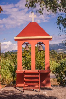 Kırsal çan kulesi iki zilli, parlak gökyüzüne karşı kırmızı yapı ve yemyeşil.