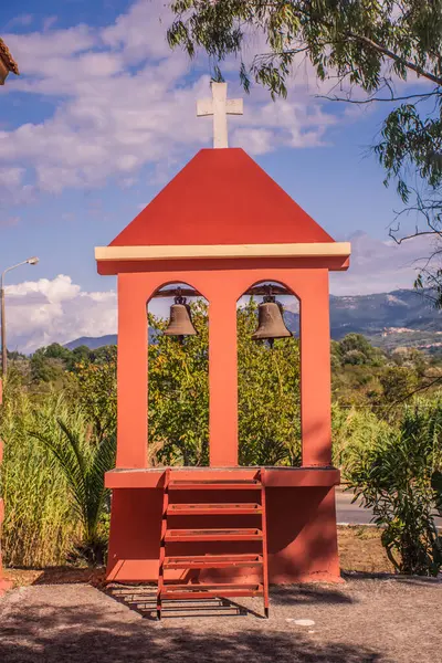 Kırsal çan kulesi iki zilli, parlak gökyüzüne karşı kırmızı yapı ve yemyeşil.