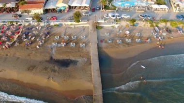 Turkuaz suya uzanan bir rıhtım manzarası, sahil şemsiyeli kumlu bir plajla karşılaşma. Yunanistan 'ın Korfu adasındaki Arillas plajı.