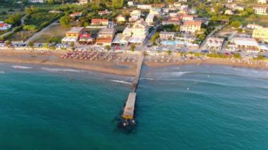 Turkuaz suya uzanan bir rıhtım manzarası, sahil şemsiyeli kumlu bir plajla karşılaşma. Yunanistan 'ın Korfu adasındaki Arillas plajı.